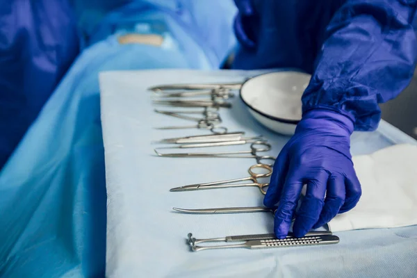 Tangan di sarung tangan biru lay out instrumen bedah di ruang operasi di atas meja. Persiapan untuk operasi. Instrumen steril — Stok Foto