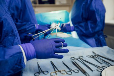 Operasyon sürecini kapat. Cerrahi aletler masaya konur, mavi eldivenli bir doktor cerrahi makas tutar. Ameliyat için hazırlık. Steril aletler