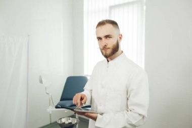 Erkek bir jinekolog ofiste tek başına elinde tabletle kameraya bakıyor. Modern tıp kavramı