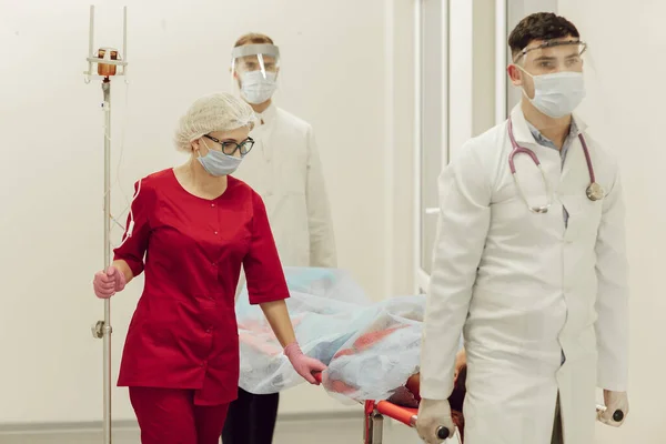 Notärzte brachten einen Patienten mit einem Coronavirus-Patienten auf einer Trage. Ärzte in Schutzanzügen bringen den Patienten ins Krankenhaus. Coronavirus-Pandemie, Lungenentzündung — Stockfoto