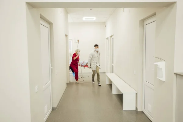 Ein Ärzteteam trägt einen kranken Patienten schnell auf einer Trage. Notärzte in Schutzmasken und Anzügen, der Patient vermutet Coronavirus. Die Arbeit von Medizinern während einer Pandemie Stockbild