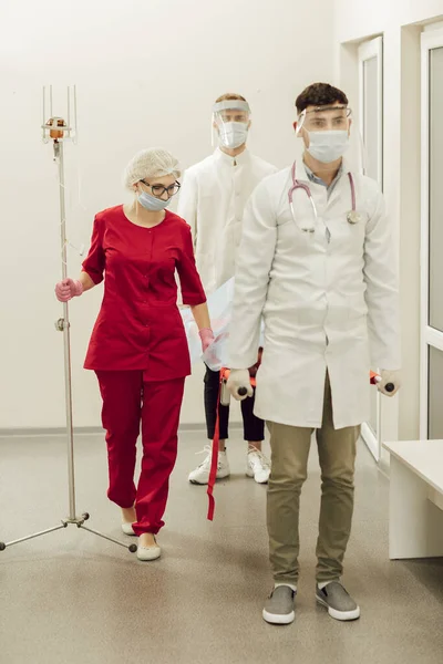 Sebuah tim dokter membawa pasien yang sakit pada tandu. Ambulans dokter dengan topeng pelindung dan jas, pasien mencurigai coronavirus. Pekerjaan medis selama pandemi. — Stok Foto