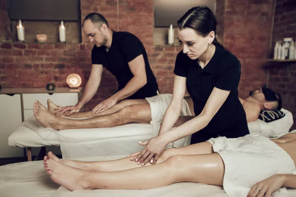 Two masseurs doing a foot massage to a young couple. Man and woman enjoying a massage in a spa salon.