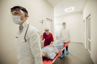 Bir grup doktor hasta bir hastayı sedyede taşıyor. Koruyucu maskeli ve takım elbiseli ambulans doktorları, hasta koronavirüsten şüpheleniyor. Bir salgın sırasında sağlık görevlilerinin çalışmaları