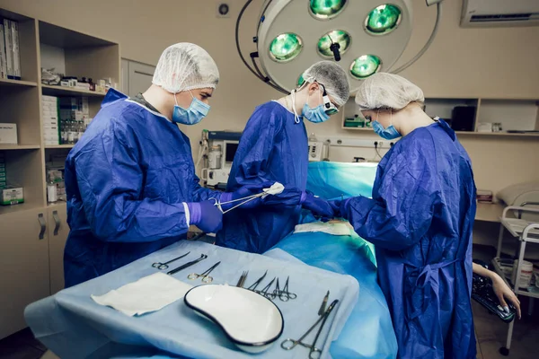 Portret van een team chirurgen aan het werk. Drie dokters in medische maskers bij operaties beginnen de patiënt te opereren. Artsen in chirurgie, behandeling en geneeskunde — Stockfoto