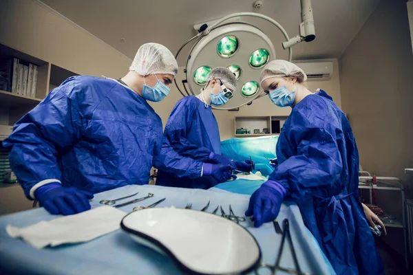 Retrato del equipo de cirujanos en el trabajo. Tres médicos con máscaras médicas en operaciones comienzan a operar al paciente. Médicos en cirugía, tratamiento y medicina Fotos De Stock Sin Royalties Gratis