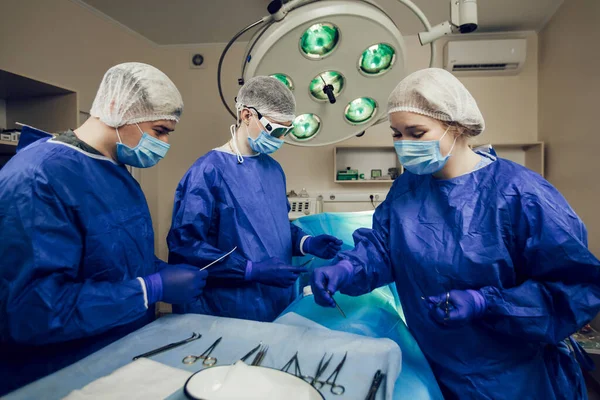 Potret tim ahli bedah di tempat kerja. Tiga dokter bertopeng medis dalam operasi mulai mengoperasi pasien. — Stok Foto