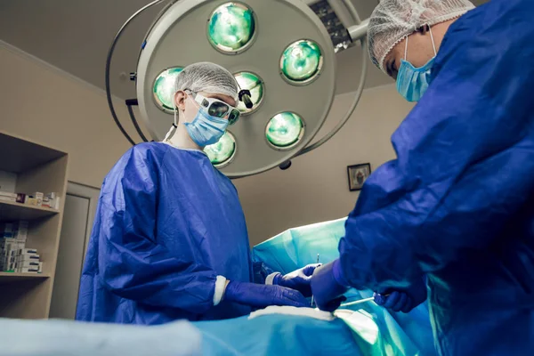 Pandangan bawah, dua ahli bedah melakukan operasi di rumah sakit. Pandangan samping dokter muda di tempat kerja. Konsep bedah — Stok Foto