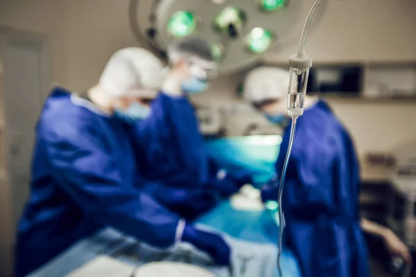 Medische dropper op de achtergrond van een team chirurgen die een operatie uitvoeren. Chirurgie in de operatiekamer, voorbereiding op de operatie — Stockfoto