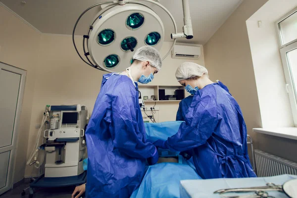 Sebuah tim ahli bedah dengan seragam biru beroperasi pada pasien di rumah sakit. Sisi tampilan dokter muda di tempat kerja — Stok Foto