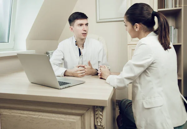 Dokter muda dan pasien duduk di meja dengan laptop di kantor rumah sakit. Dokter berbicara kepada pasien wanita muda. Konsep pengobatan, pencegahan kesehatan — Stok Foto