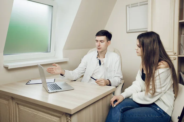 Dokter muda dan pasien duduk di meja dengan laptop di kantor rumah sakit. Dokter berbicara kepada pasien wanita muda. Konsultasikan ke dokter sebelum operasi. — Stok Foto