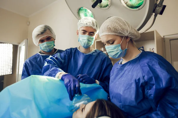 Anestesi pasien sebelum operasi. Tiga ahli bedah di tempat kerja. Dokter sedang mempersiapkan operasi. Ahli bedah dan pasien di rumah sakit — Stok Foto