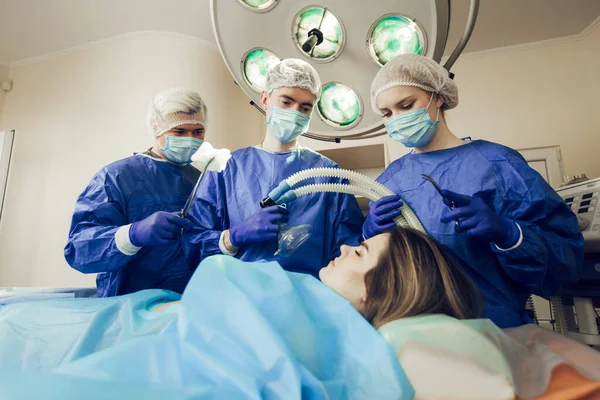 A beteg altatása műtét előtt. Három sebész dolgozik. Az orvosok készülnek a műtétre. Sebészek és egy beteg a kórházban Stock Fotó