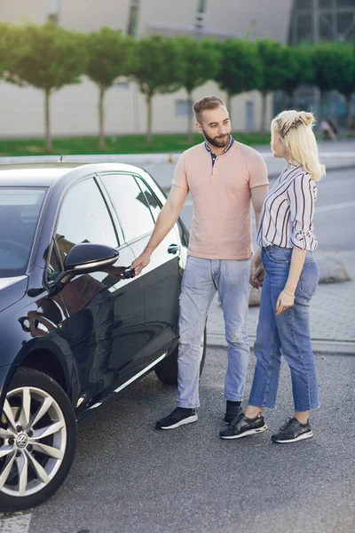 남자는 새 차를 구입 함으로써 여자를 놀라게 한다. 야외에 있는 새 차 근처에서 행복 한 젊은 부부. 차를 사는 일 — 스톡 사진