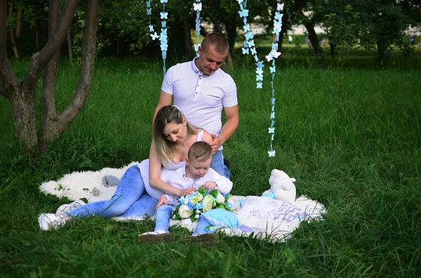 Happy family together in summer garden/park. All of them sitting in a white carpet in garden.  Outdoor photo