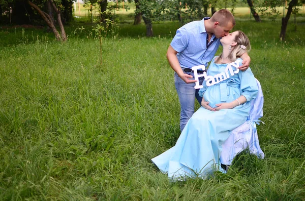 Happy family together in summer garden/park.Couple waiting for a baby. husband and wife kissing. Husband holding inscription \