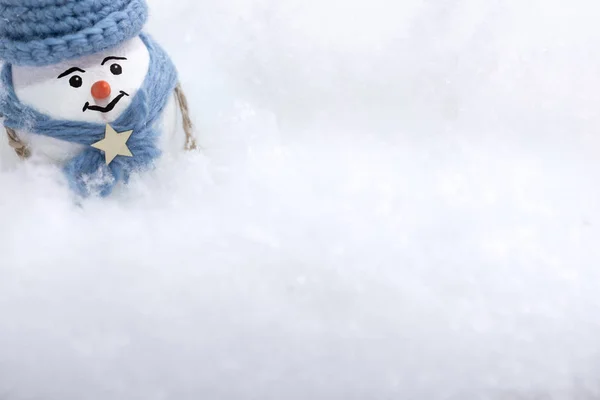 A little snowman in a blue hat and scarf is standing in a snowdrift of snow