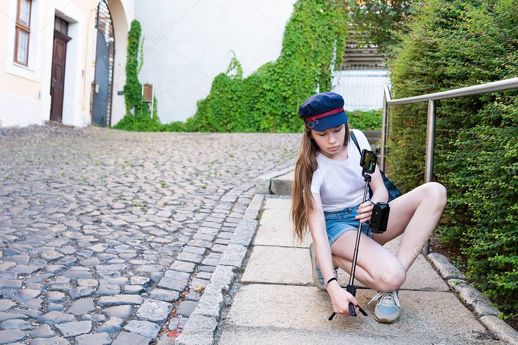 A girl with long hair sets a tripod with a telephone on the street