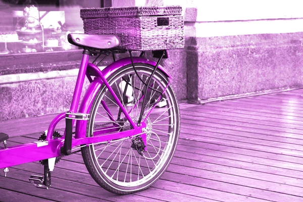 Vista de uma bicicleta rosa brilhante com uma cesta no chão de madeira do lado de fora . — Fotografia de Stock