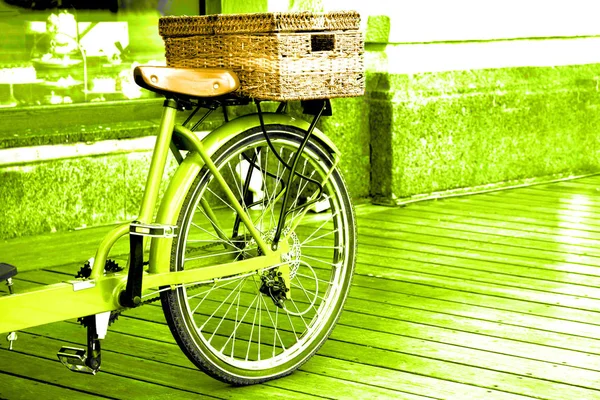 View of a green bicycle with a basket standing on the wooden floor near the building. — Stock Photo, Image