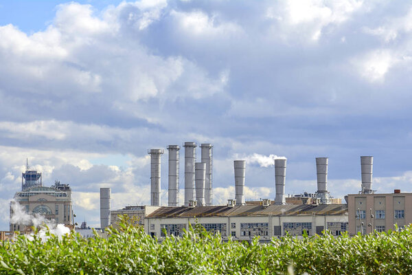View of the pipes of the plant from which there is white smoke against the sky
