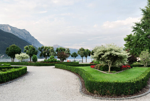 View of the mountains, the lake and the embankment of the city with trimmed trees, shrubs, lawn and flower beds