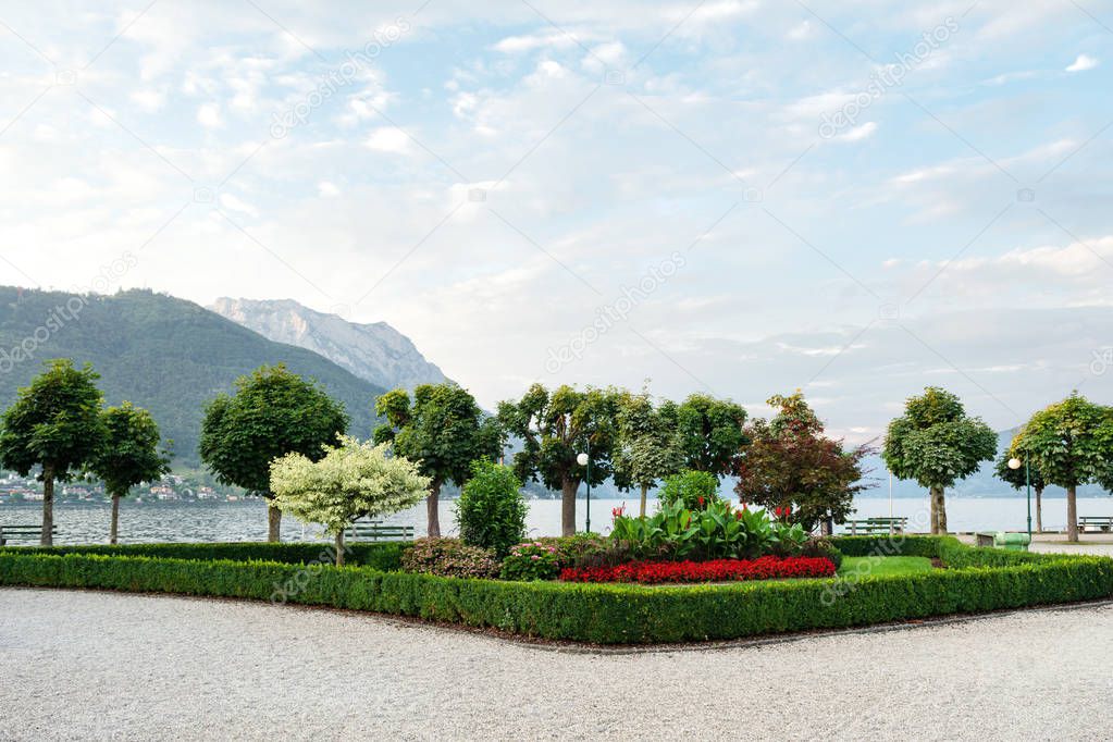 View of the mountains, the lake and the embankment of the city with trimmed trees, shrubs and flower beds.