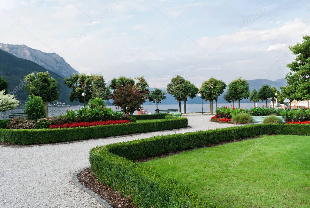 View of the mountains, the lake and the embankment of the city with trimmed trees, shrubs, lawn and flower beds.