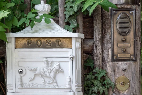 Une boîte aux lettres en métal blanc avec des éléments décoratifs est accrochée à la clôture à côté de la cloche et de l'interphone . — Photo