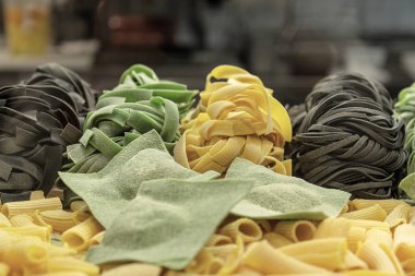 Fresh uncooked pasta and homemade ravioli with spinach and cuttlefish ink are rolled up on the table. clipart