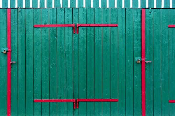 Drzwi garażowe w kolorze zielonym ozdobione są jasnymi, czerwonymi metalowymi wkładkami i białymi listwami. — Zdjęcie stockowe