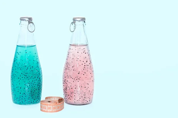 Un centimetro e bottiglie di vetro con semi di basilico blu e rosa poggiano su uno sfondo blu . — Foto Stock