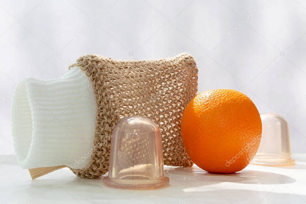 An orange is on the table and next to it are vacuum cans and a mesh washcloth made from natural fibers.
