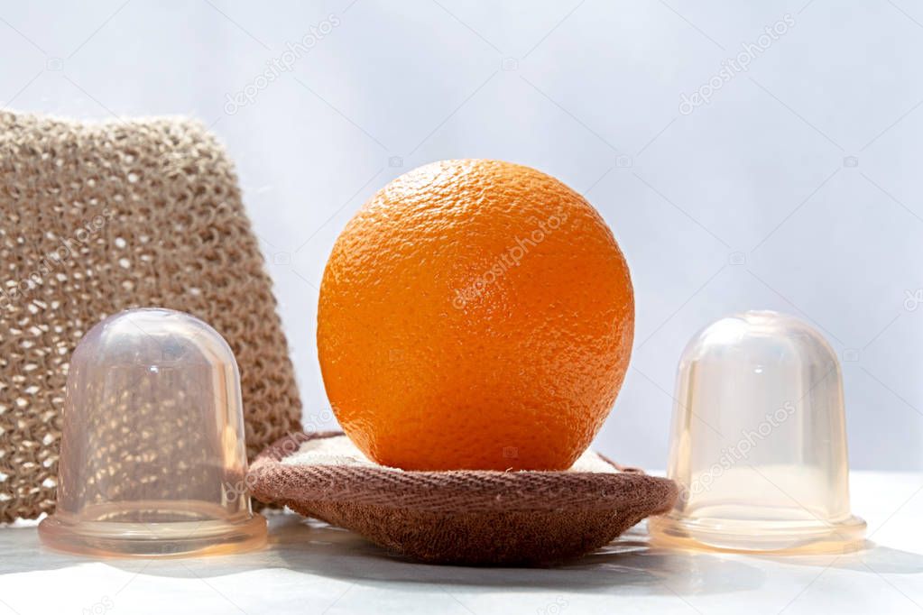 The orange is lying on a sponge made from natural fibers and there are some vacuum cans and a mesh sponge next to it.