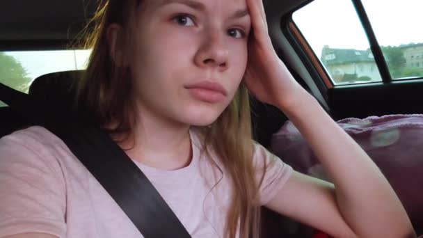 女孩坐在汽车的后座上 系着安全带 对某事不满 四处思考和环顾四周 移动着眉毛和嘴唇 汽车不动 — 图库视频影像