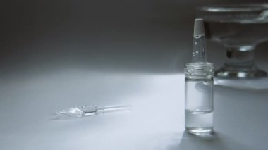 Peynir altı suyu dolu bir pipet ile bir cam şişe bir masada ve cam kap arka planda su sallanan.