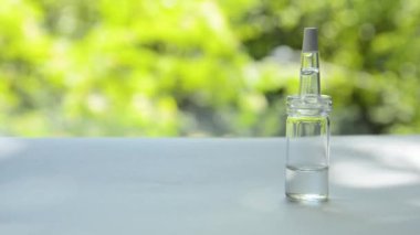 Peynir altı suyu yla dolu pipetli cam şişe, rüzgardan sallanan ağaçların arka planına karşı beyaz bir masanın üzerinde duruyor.