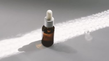 Beyaz yüzeyüzerinde kozmetik ile koyu pipet ile bir şişe. Güneş onun üzerinde parlıyor..