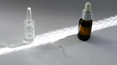 Beyaz yüzeyde bir kozmetik ile koyu ve açık cam pipetler ile şişeler vardır. Güneş üzerlerinde parlıyor. Aralarında cam çubuk dönüyor ve duruyor beyaz bir şişe yi gösteriyor.