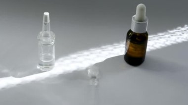 Beyaz yüzeyde bir kozmetik ile koyu ve açık cam pipetler ile şişeler vardır. Güneş üzerlerinde parlıyor. Aralarında cam çubuk dönüyor ve duruyor beyaz bir şişe yi gösteriyor.