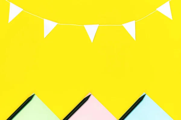 The layout of the colored paper, black pencils and a garland of white flags located on a yellow background. — Stock Photo, Image