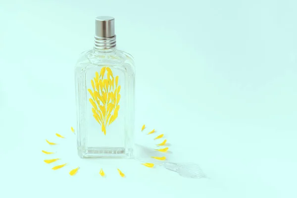 Transparante Parfum Fles Een Blauwe Achtergrond Versierd Met Gele Bloemblaadjes — Stockfoto