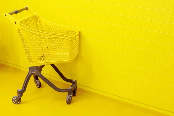 购物的概念 一辆空黄色的杂货车站在黄色的地板上 背景是一面黄色的墙 — 图库照片
