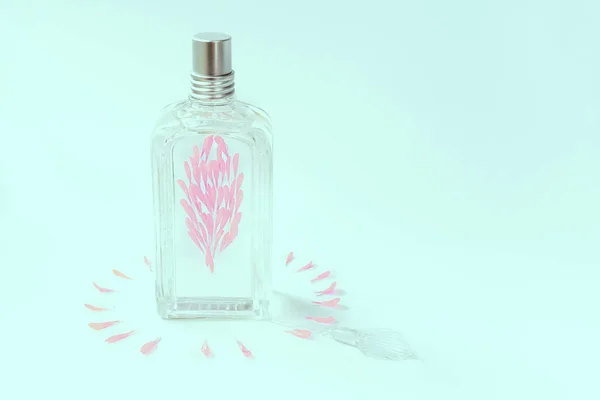 Frasco de perfume transparente sobre fondo azul decorado con pétalos de flores rosadas . — Foto de Stock