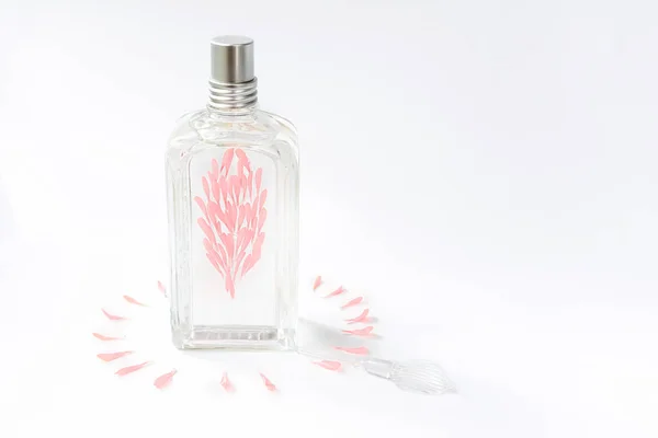 Átlátszó parfümös üveg fehér alapon rózsaszín virágszirmokkal díszítve. — Stock Fotó