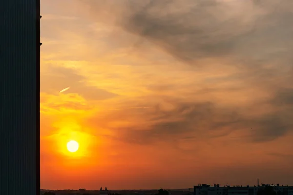 Ciudad. La puesta de sol en el cielo es de color rojo-naranja con nubes grises en forma de manchas en las que brilla el sol . —  Fotos de Stock