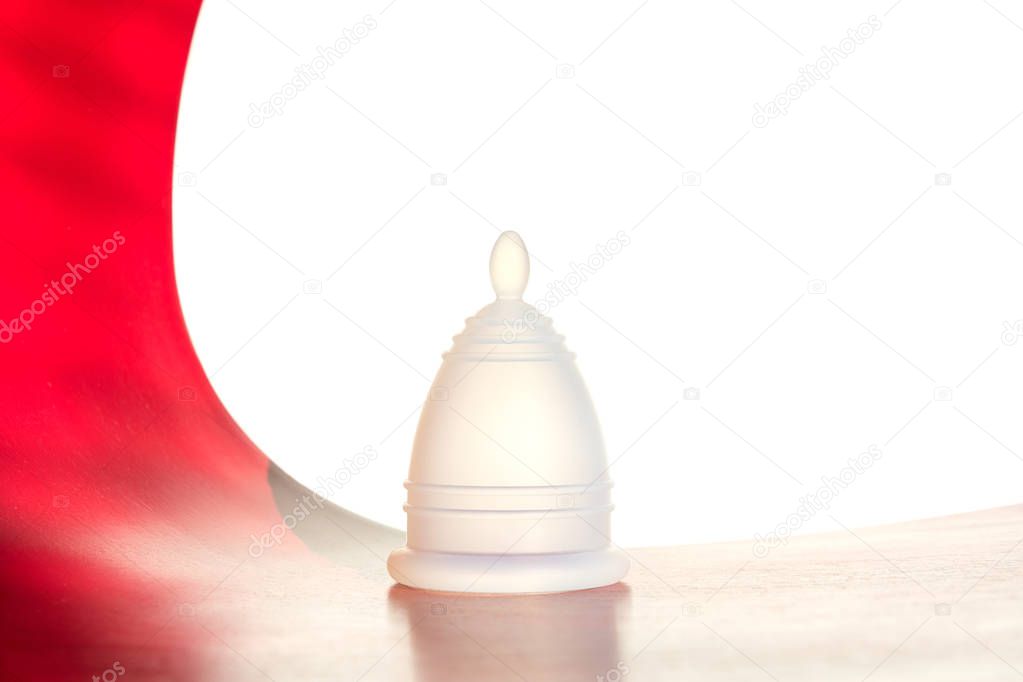 White reusable menstrual cup on a white-red background.