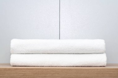 İki düzgünce katlanmış beyaz havlu seramik karobir arka plan karşı ahşap bir raf üzerinde yalan.