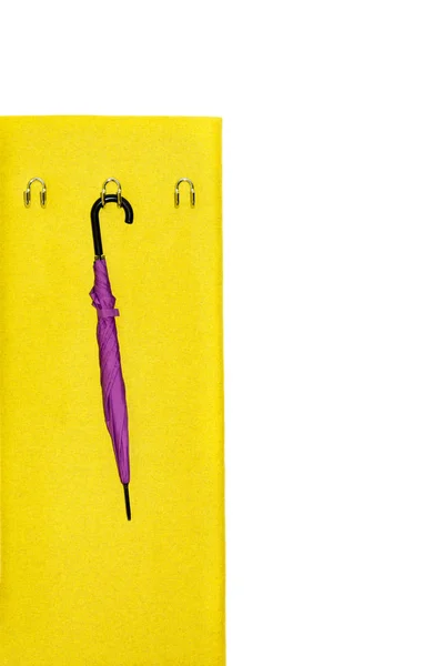 A folded purple umbrella hangs on a hook in a yellow hallway against a white wall. Concept interior, order in the house.